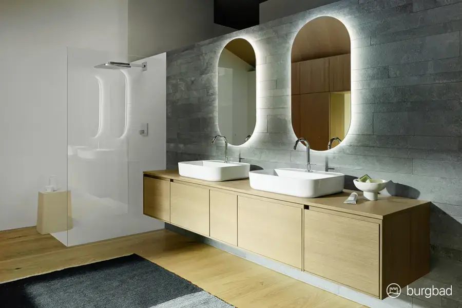 Modernes Designbad mit Doppelwaschtisch, beleuchteten Spiegeln und bodengleicher Dusche – hochwertige Badplanung von Der Bäderbauer